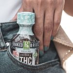 a small bottle of Baked Bros pourable THC syrup inserted in a person's denim jeans side pocket