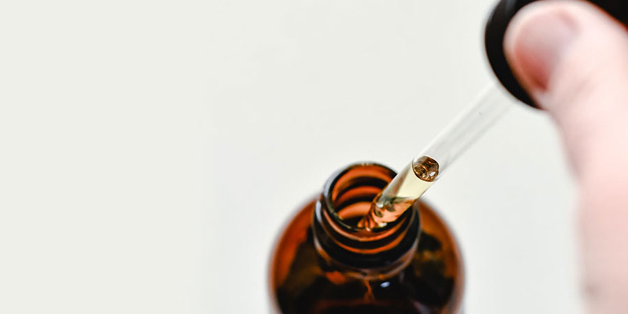 close up view of a small brown glass bottle and a person's hand holding a dropper with THC oil